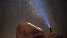 Illustration of a person shining a light toward the stars to accompany the article Three Rational Proofs God Exists