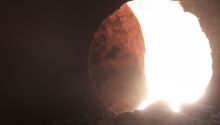 View from inside a tomb looking toward a round opening with the round stone door mostly rolled back. This illustrates the article 